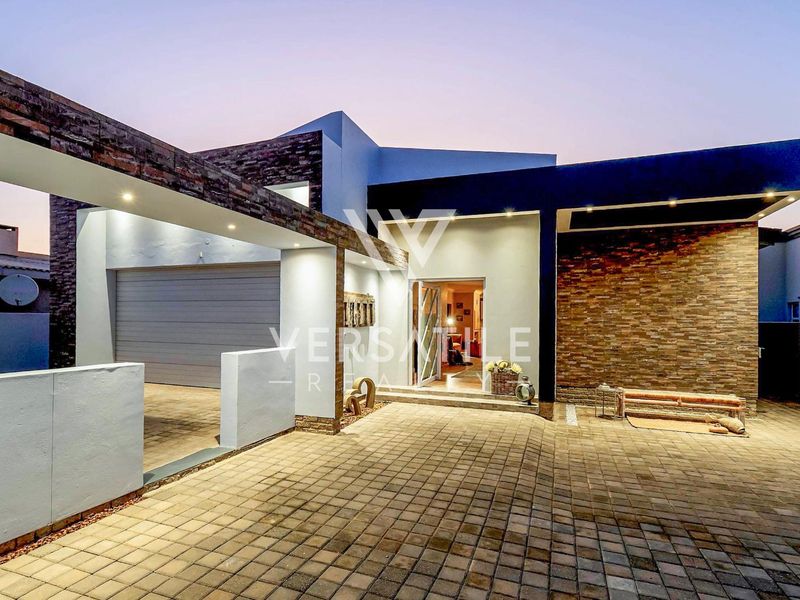 Modern front facade featuring stone cladding, a paved driveway, covered entrance, and integrated garage, showcasing contemporary architectural design and well-maintained exterior finishes.