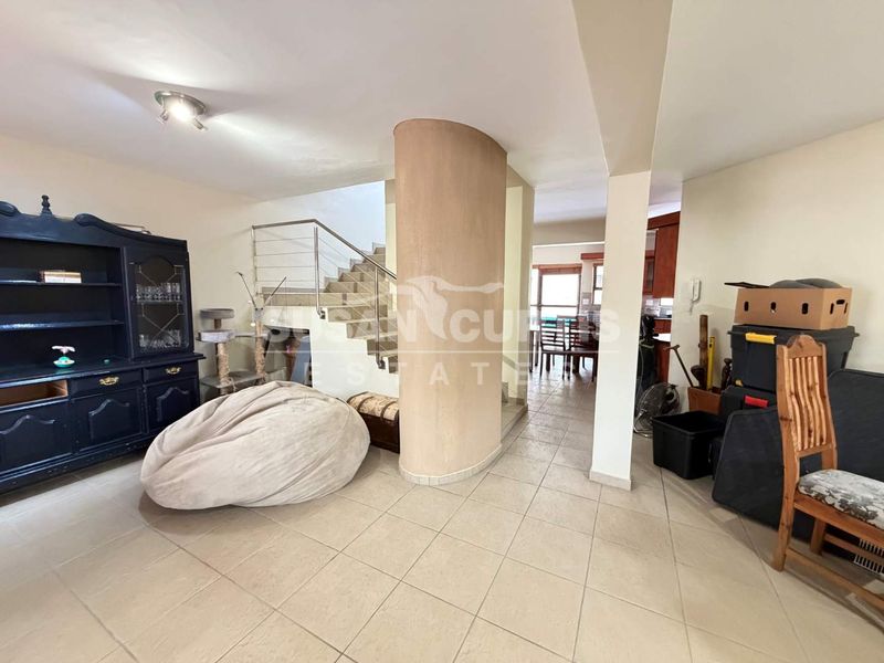 Open plan living area featuring tiled flooring, a central structural column, and a staircase with a modern stainless steel railing.
