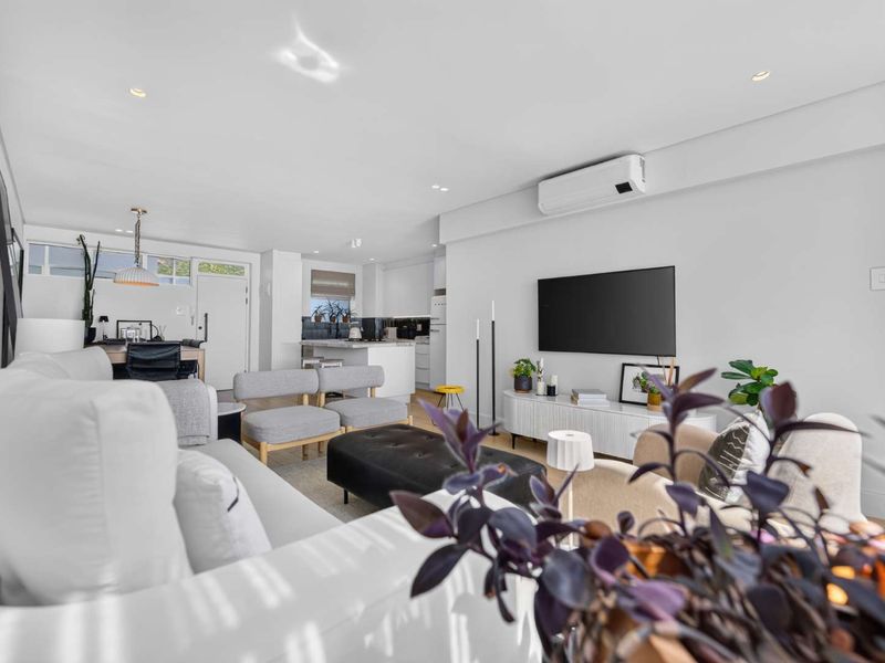 A bright and modern open-plan living and kitchen area featuring recessed lighting, a split-system air conditioner, and a contemporary kitchen island.