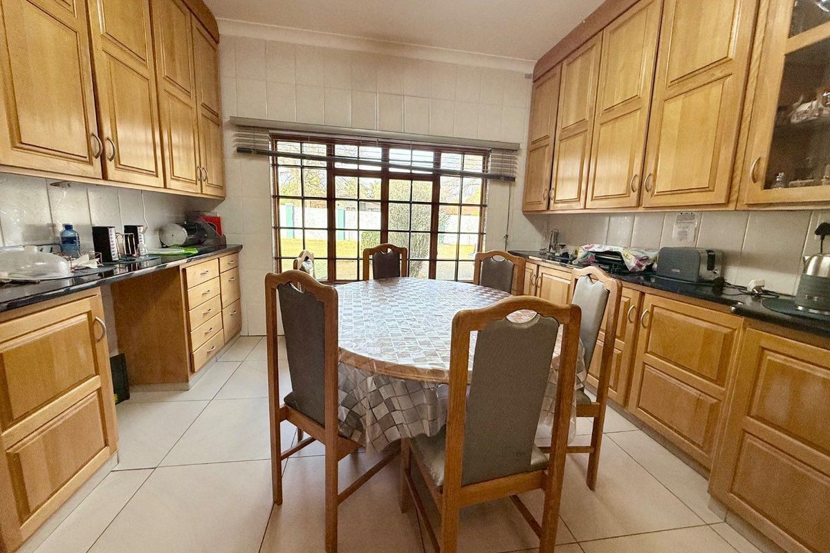 A functional kitchen featuring extensive light wood cabinetry, dark countertops, tiled flooring, and a dedicated dining area with natural light from the rear window.