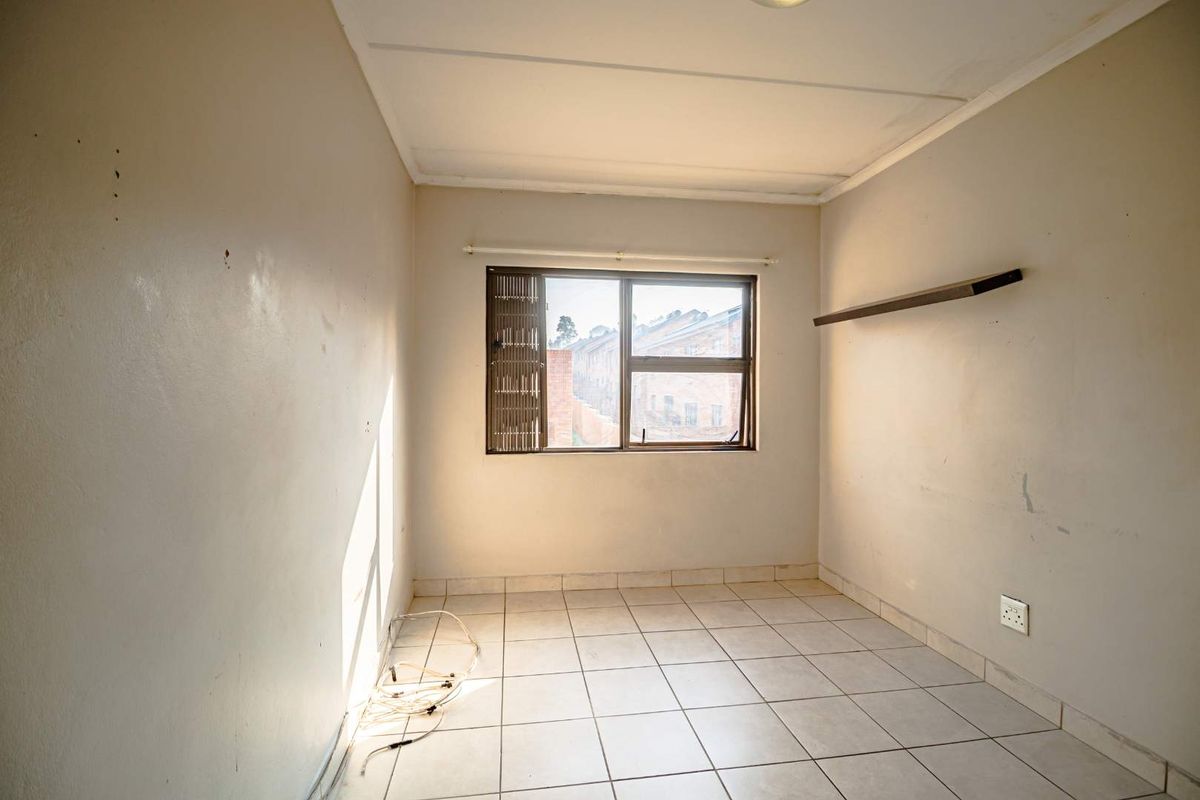 A vacant bedroom featuring tiled flooring, a single window with security bars, and a wall-mounted shelf.