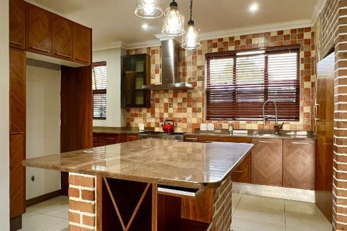 A well-appointed kitchen featuring a central stone-topped island with built-in wine storage, wooden cabinetry, tiled backsplash, and stainless steel extractor fan.