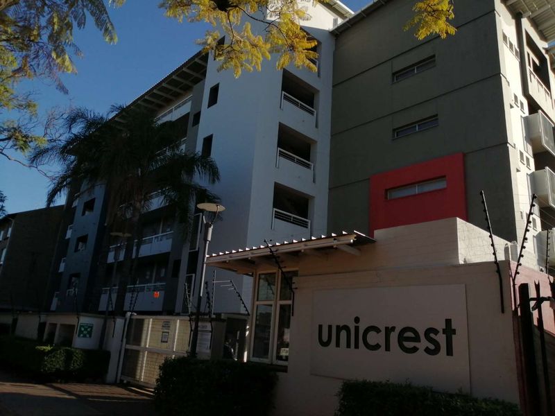 Exterior view of the Unicrest apartment complex featuring multi-story residential units with balconies and secure gated entrance.