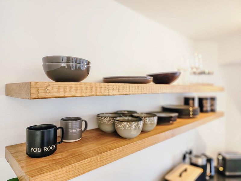 Close-up view of modern floating timber shelving installed in the kitchen area, providing functional open storage space.