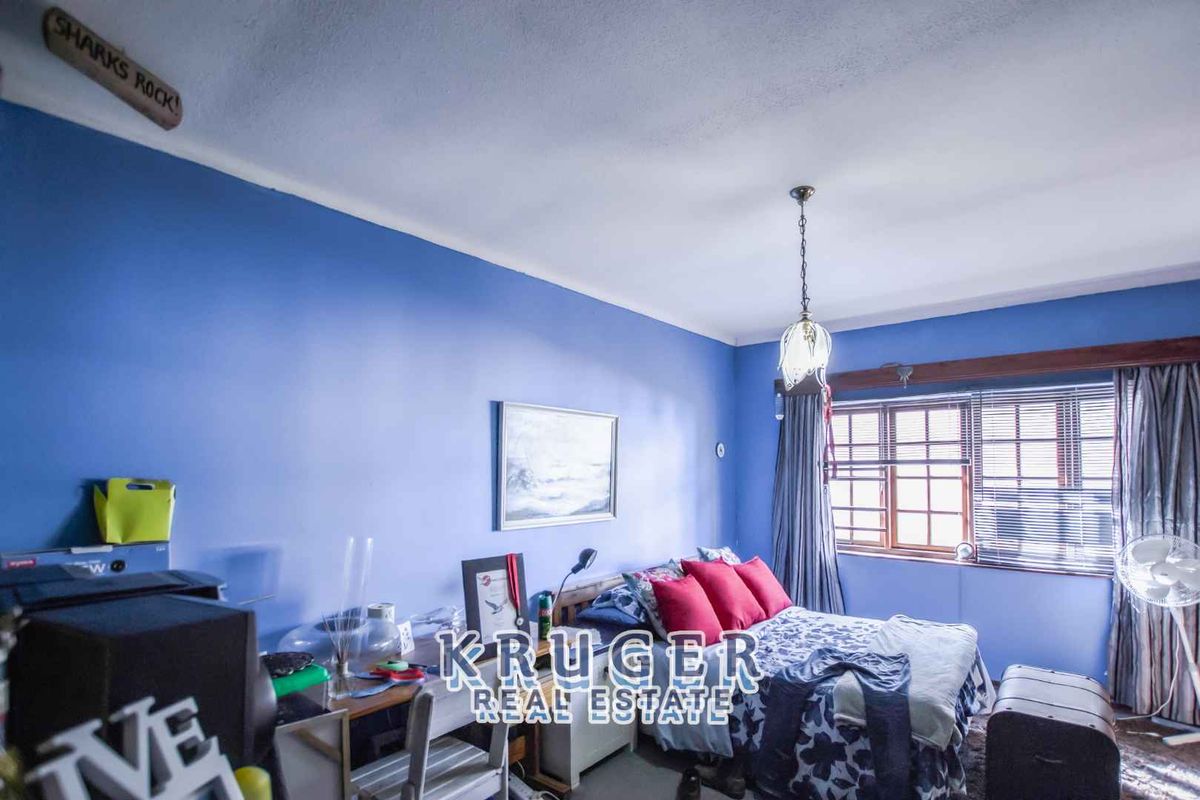 A bedroom featuring blue painted walls, a wooden window frame with blinds, and a central pendant light fixture.