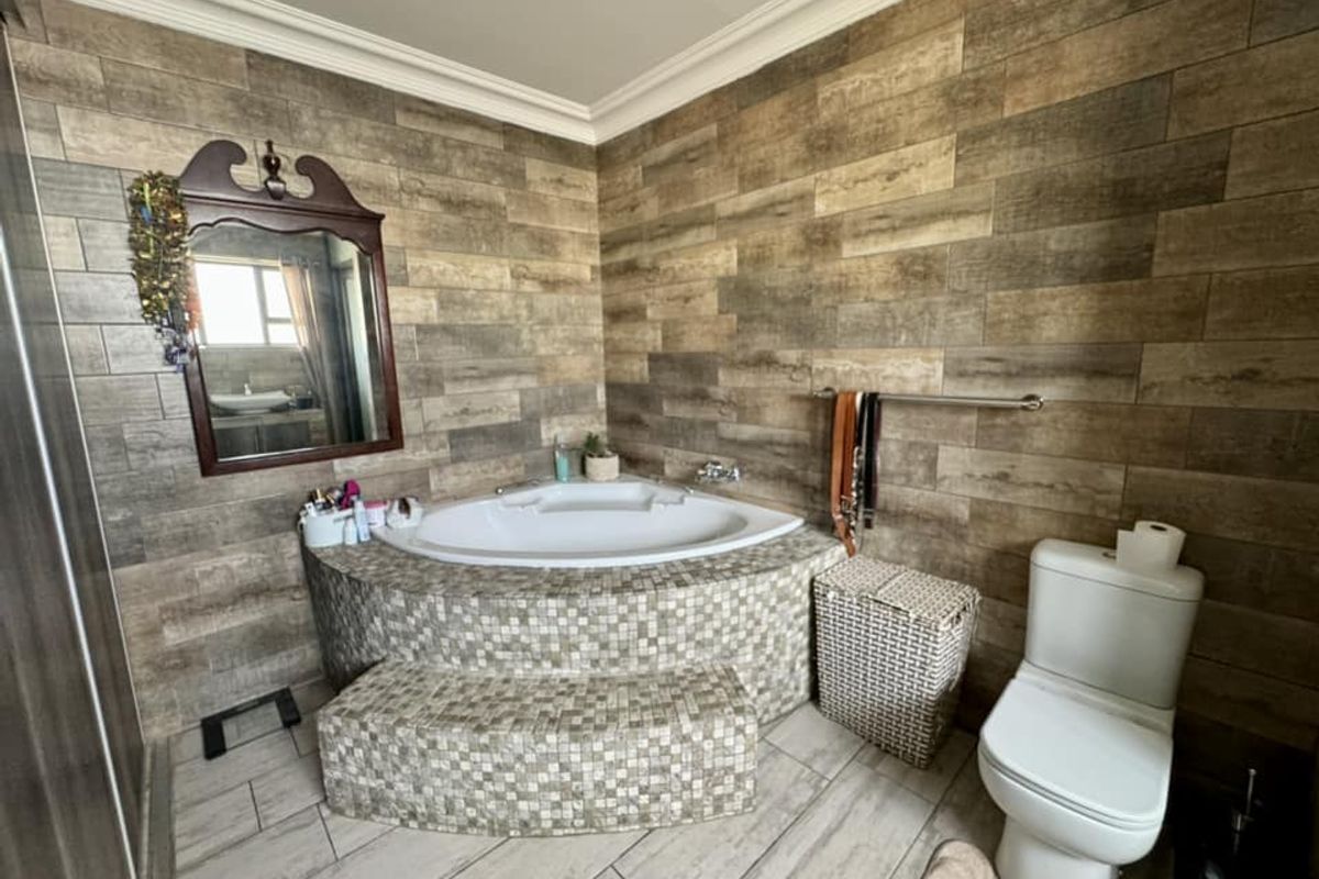 Bathroom featuring a corner soaking tub with mosaic tile surround, wood-look wall tiling, and a standard toilet.