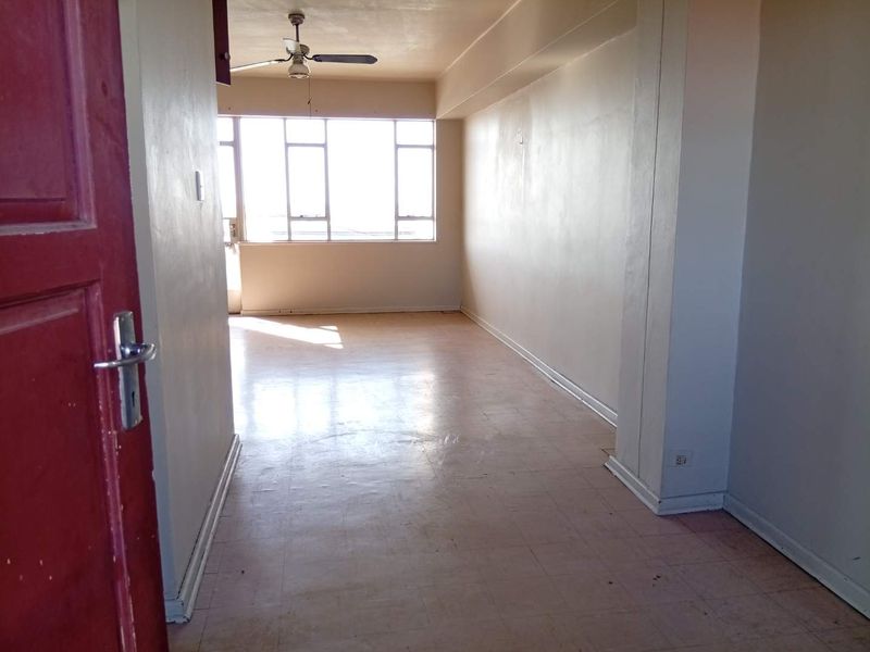 An empty, sunlit living area featuring tiled flooring, a ceiling fan, and large windows, offering a blank canvas for renovation.
