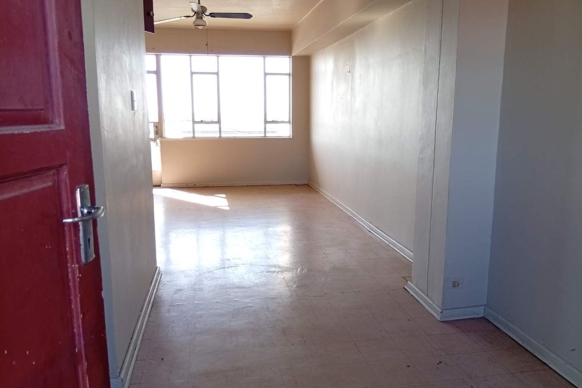 An empty, sunlit living area featuring tiled flooring, a ceiling fan, and large windows, offering a blank canvas for renovation.