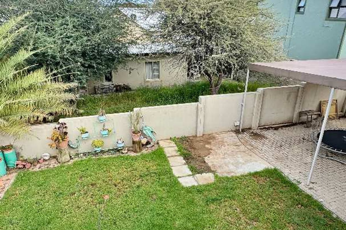 A rear garden featuring a lawn area, paved patio section with a fixed shade structure, and perimeter boundary walling.