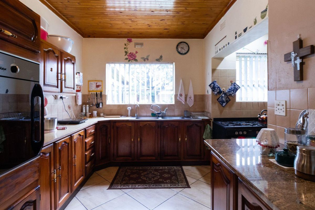 A traditional kitchen featuring dark wood cabinetry, granite countertops, a built-in oven, and a distinctive timber-paneled ceiling.