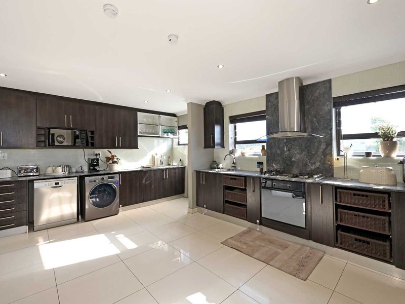 Modern kitchen featuring dark wood cabinetry, stone countertops, stainless steel appliances, gas hob, and tiled flooring with ample storage space.