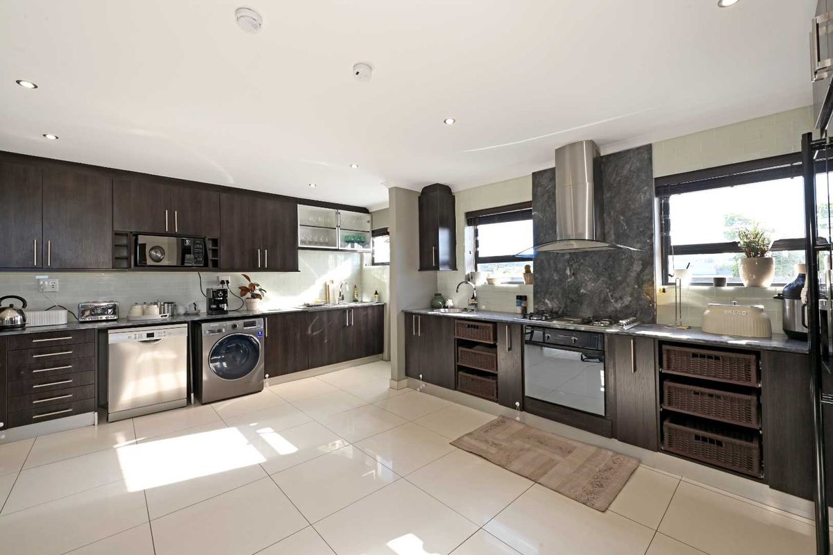 Modern kitchen featuring dark wood cabinetry, stone countertops, stainless steel appliances, gas hob, and tiled flooring with ample storage space.
