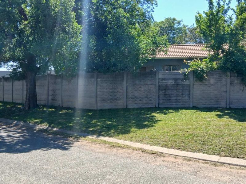 Street view showing the asphalt road, curb, and the precast concrete boundary wall surrounding the property.