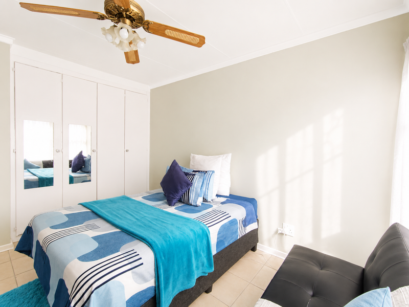 A bedroom featuring built-in cupboards with mirrored panels, a ceiling fan, and tiled flooring, offering a functional and well-lit living space.