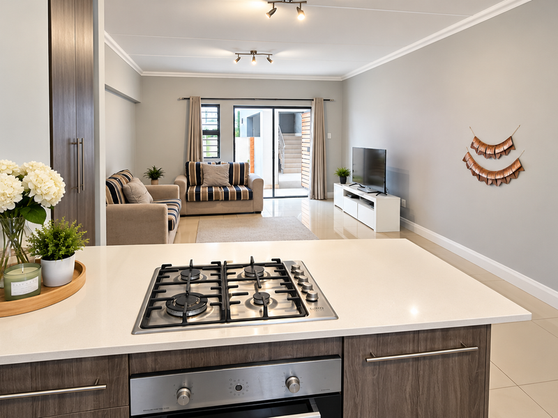 Modern open-plan living area featuring a sleek kitchen with gas hob, built-in oven, and quartz countertops, flowing seamlessly into a bright, tiled lounge space.