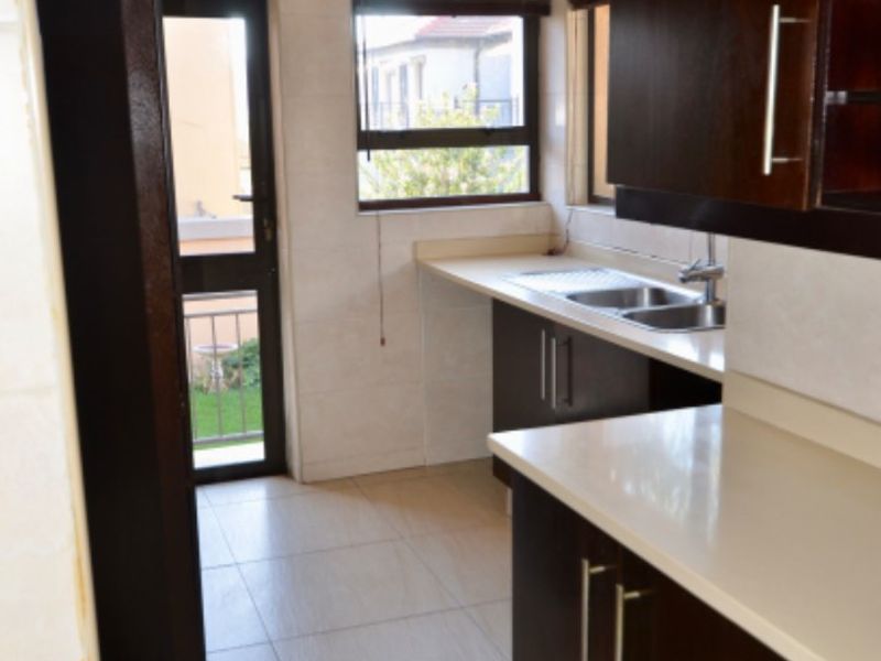 A clean, functional kitchen featuring dark wood cabinetry, light stone countertops, tiled finishes, and direct access to an outdoor area.