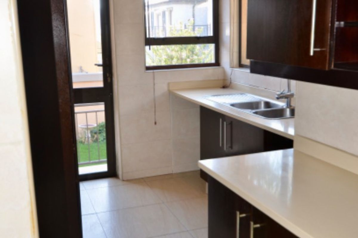 A clean, functional kitchen featuring dark wood cabinetry, light stone countertops, tiled finishes, and direct access to an outdoor area.