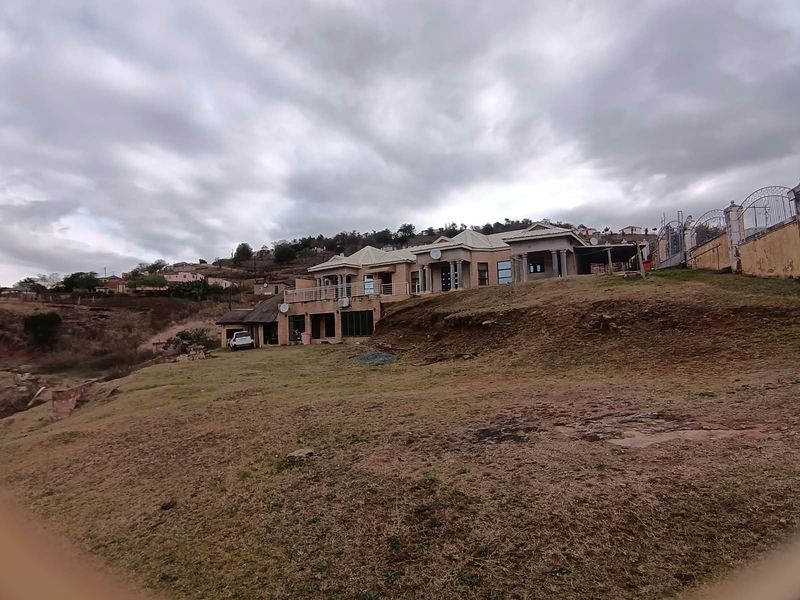 A wide-angle view of the rear elevation of a large residential property featuring a balcony, columns, and extensive surrounding grounds.