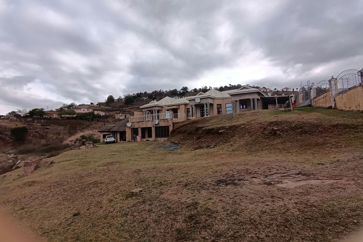 A wide-angle view of the rear elevation of a large residential property featuring a balcony, columns, and extensive surrounding grounds.