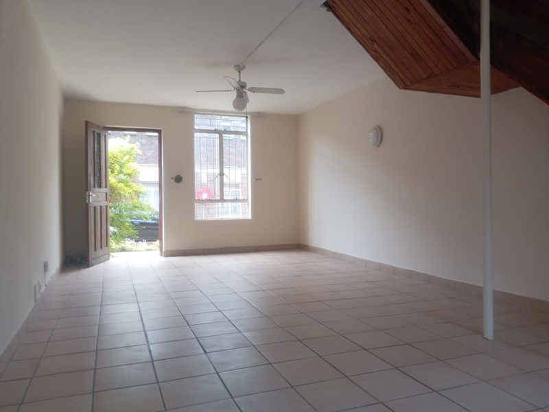 An open-plan living area featuring tiled flooring, a ceiling fan, and a timber staircase leading to the upper level.