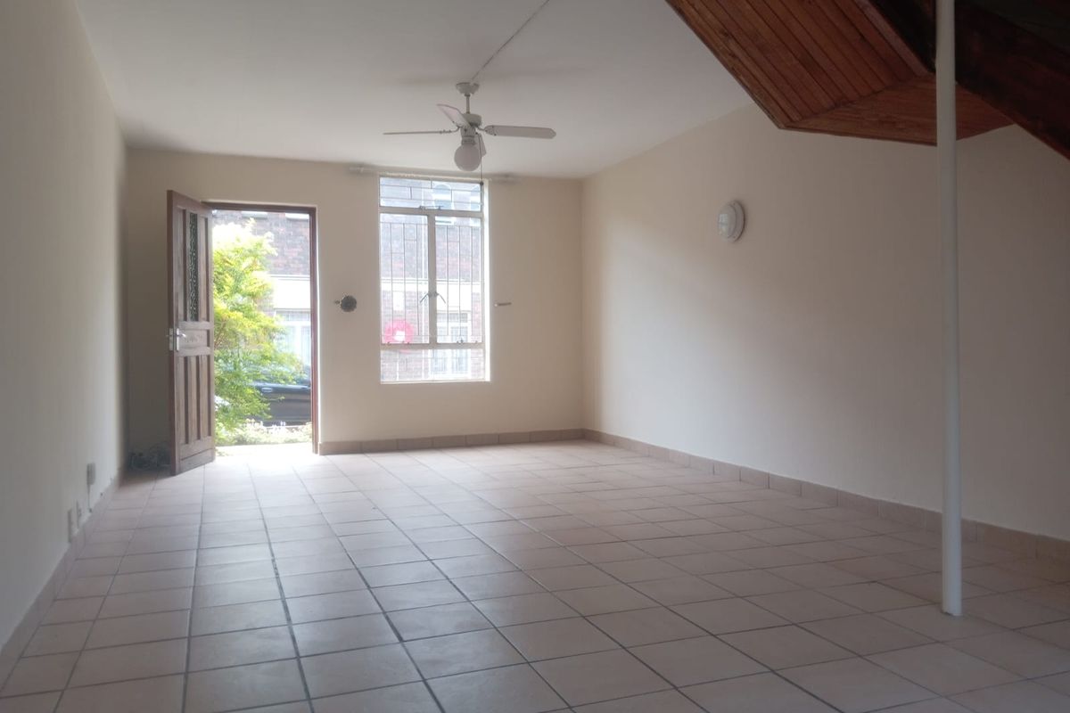 An open-plan living area featuring tiled flooring, a ceiling fan, and a timber staircase leading to the upper level.