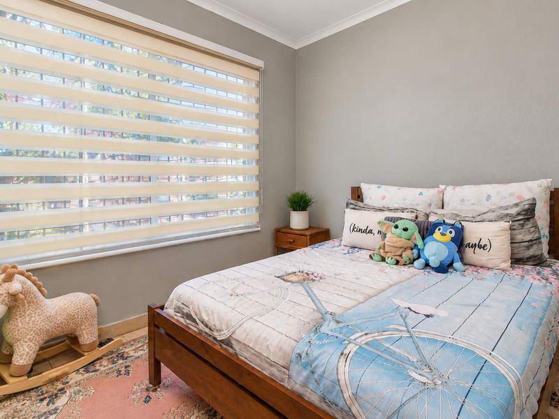 A well-maintained bedroom featuring neutral grey walls, tiled flooring, and modern zebra blinds, providing a clean and functional living space.