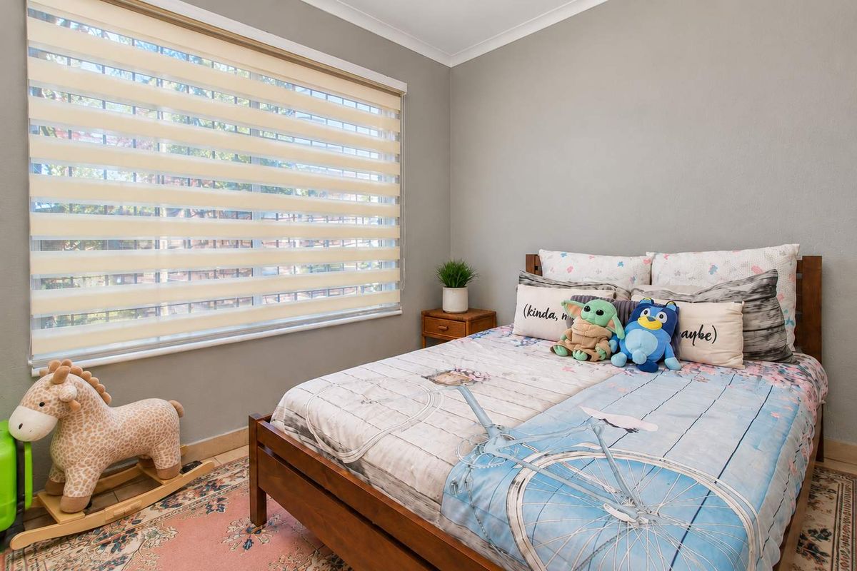 A well-maintained bedroom featuring neutral grey walls, tiled flooring, and modern zebra blinds, providing a clean and functional living space.