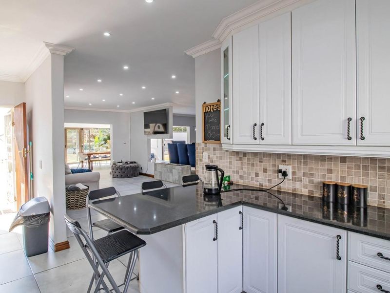 Open-plan kitchen featuring granite countertops, tiled backsplash, and white cabinetry, flowing seamlessly into a spacious living area with recessed lighting.