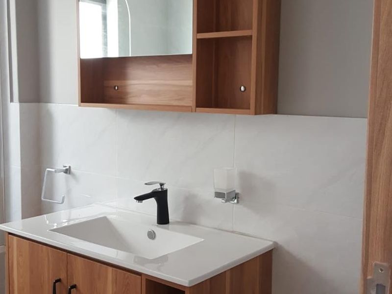 A modern bathroom vanity featuring a wood-finish cabinet, integrated sink, black faucet, and matching wall-mounted mirror cabinet with open shelving.