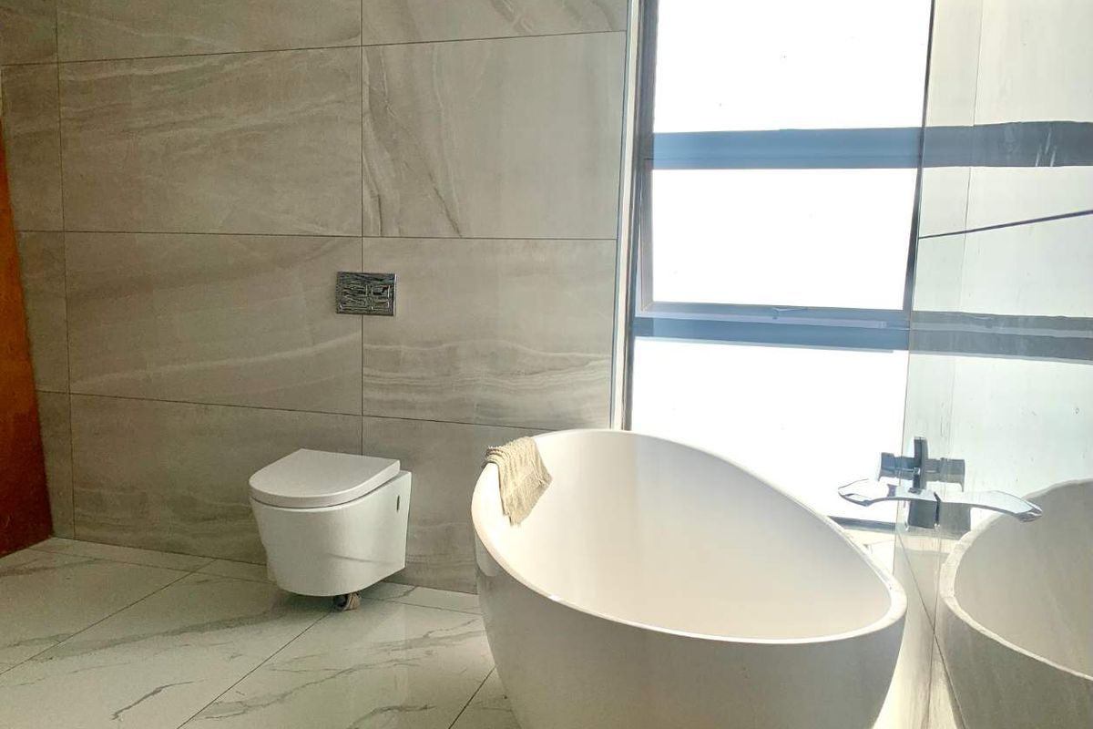 Modern bathroom featuring a sleek freestanding bathtub, wall-mounted toilet, and high-end large format tiling throughout.