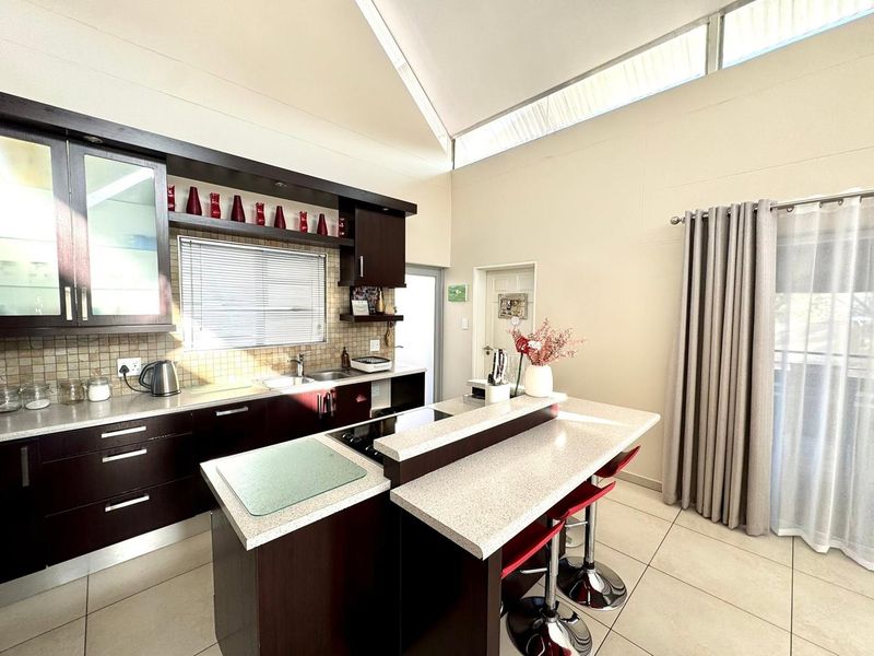 Modern kitchen featuring dark wood cabinetry, stone countertops, a central island with a built-in hob, and high ceilings with clerestory windows for natural light.