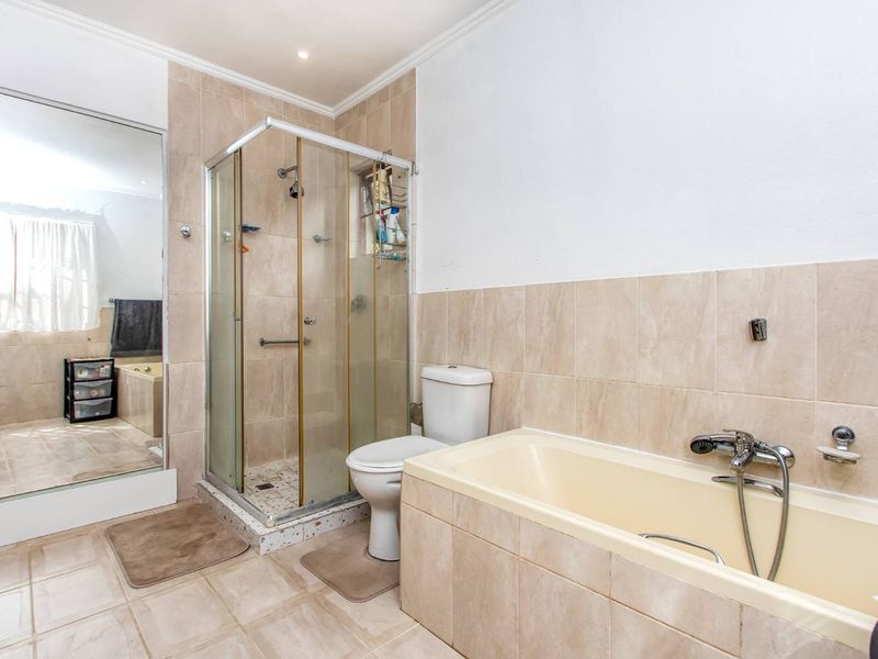 A functional bathroom featuring a shower enclosure, bathtub, toilet, and neutral wall and floor tiling.