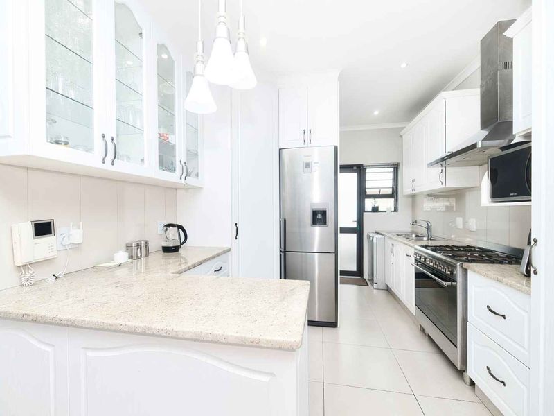 Modern, well-lit kitchen featuring white cabinetry, granite countertops, a gas stove with extractor fan, and tiled flooring, offering a clean and functional workspace.