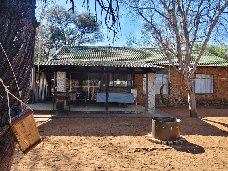 Rear view of the house featuring a covered patio, stone exterior walls, tiled roof, and a spacious garden area with a fire pit.