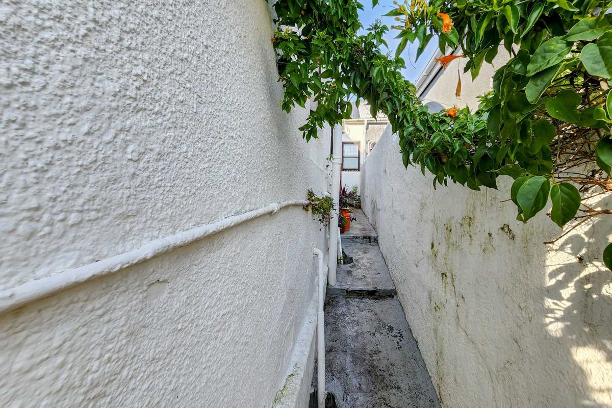 A narrow side passage or exterior walkway featuring textured walls, concrete flooring, and exposed utility piping.