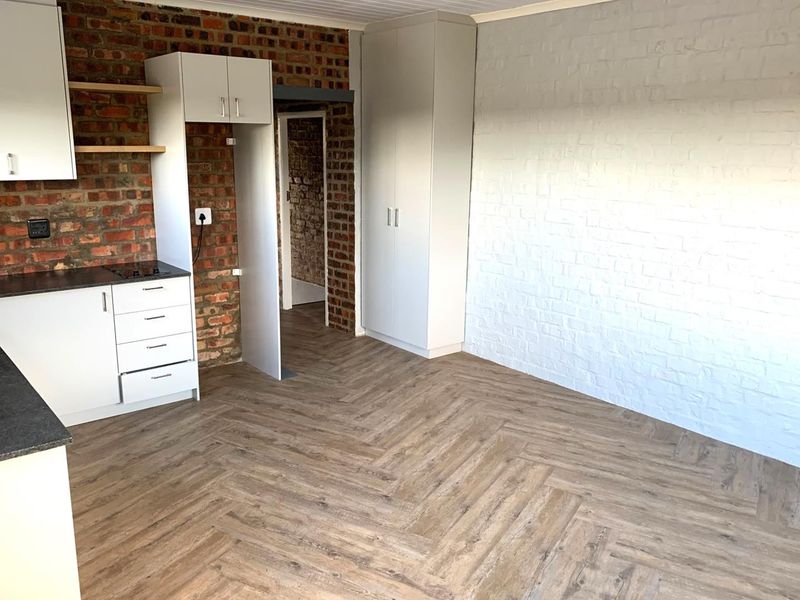Open-plan living area featuring a modern kitchen with built-in cabinetry, hob, and stylish herringbone laminate flooring, complemented by exposed and painted brick walls.