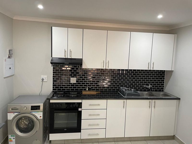 A modern kitchen featuring white cabinetry, black subway tile backsplash, granite countertops, integrated oven, gas hob, and a double sink.