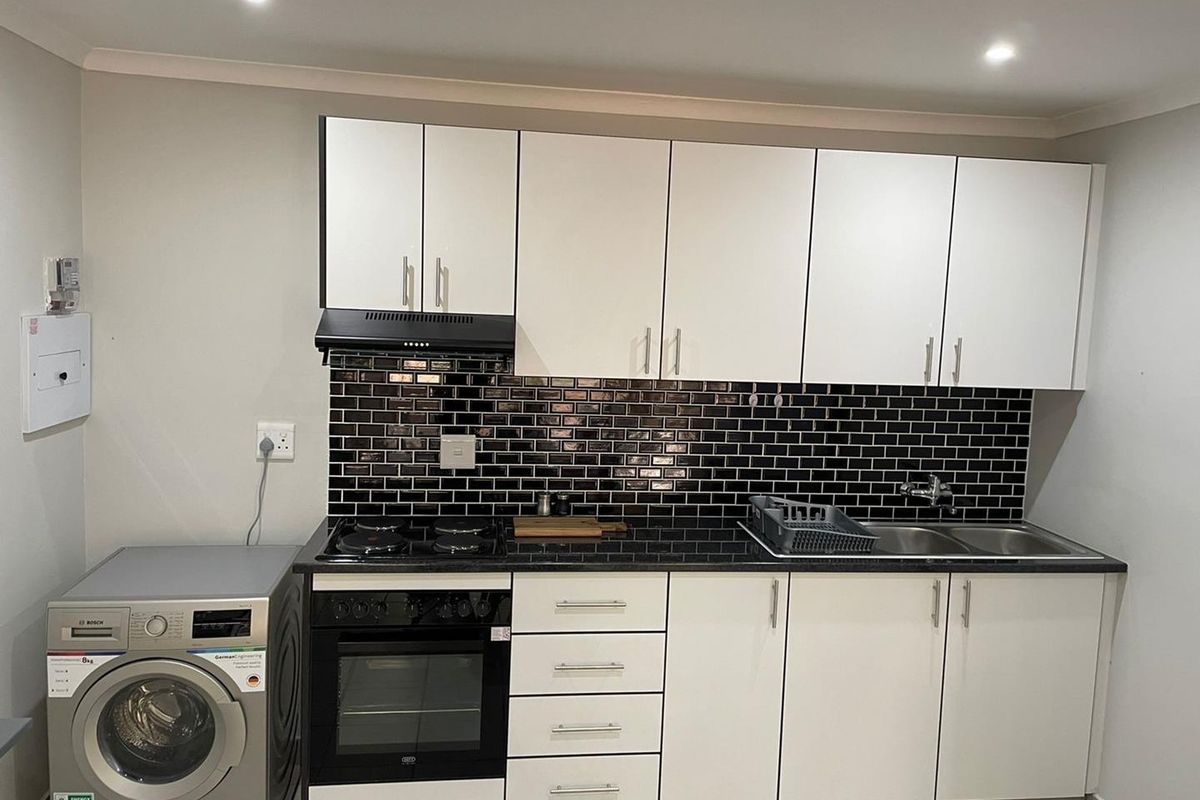 A modern kitchen featuring white cabinetry, black subway tile backsplash, granite countertops, integrated oven, gas hob, and a double sink.