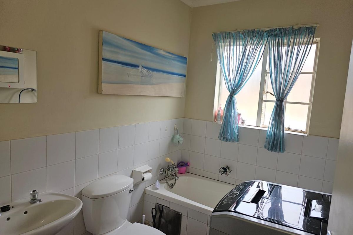 A functional bathroom featuring a white bathtub, pedestal basin, and toilet, with half-tiled walls and a window providing natural light.