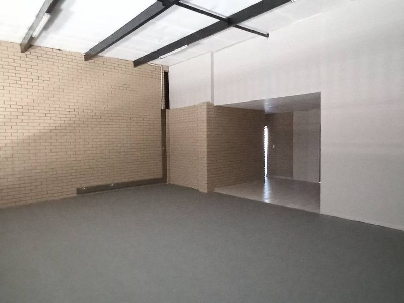 Spacious industrial open-plan area featuring exposed steel beams, brick feature walls, and durable flooring, suitable for versatile commercial or warehouse use.
