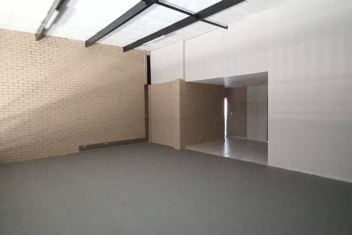Spacious industrial open-plan area featuring exposed steel beams, brick feature walls, and durable flooring, suitable for versatile commercial or warehouse use.