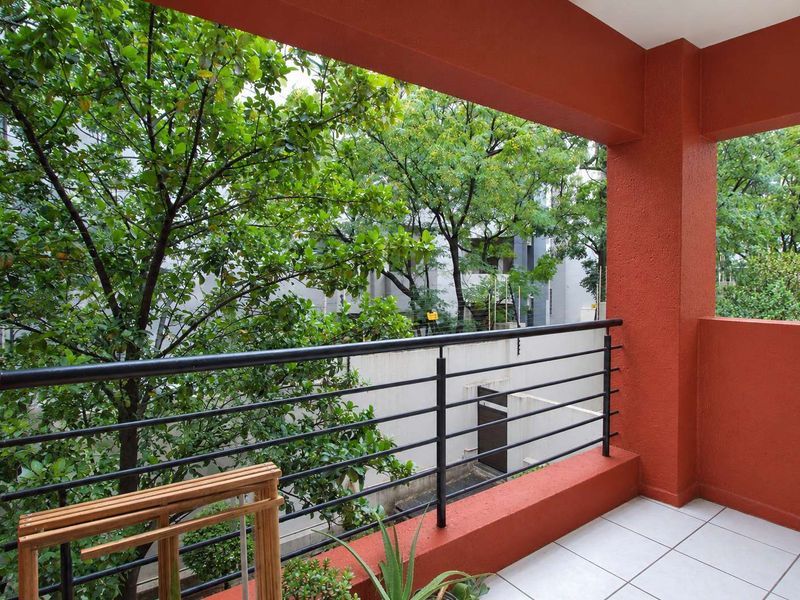 A covered balcony featuring tiled flooring, a black metal safety railing, and vibrant red painted structural pillars overlooking mature trees.