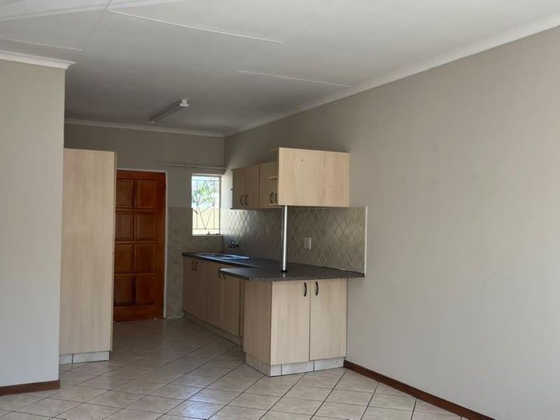 A functional, empty kitchen featuring light wood-finish cabinetry, laminate countertops, tiled backsplash, and neutral tiled flooring in a townhouse setting.