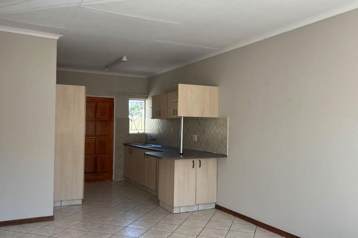 A functional, empty kitchen featuring light wood-finish cabinetry, laminate countertops, tiled backsplash, and neutral tiled flooring in a townhouse setting.