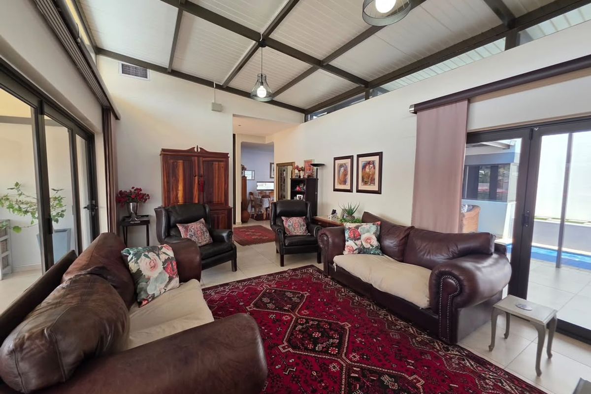 Spacious living room featuring an exposed beam ceiling, tiled flooring, and large sliding glass doors that provide seamless access to the outdoor patio area.