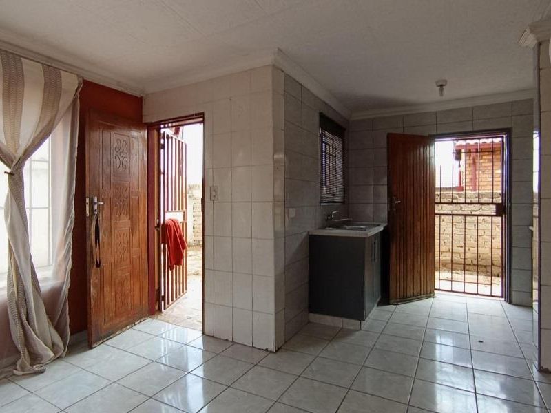 A functional kitchen area featuring tiled walls and flooring, built-in cabinetry with a sink, and direct access to the exterior via security gates.