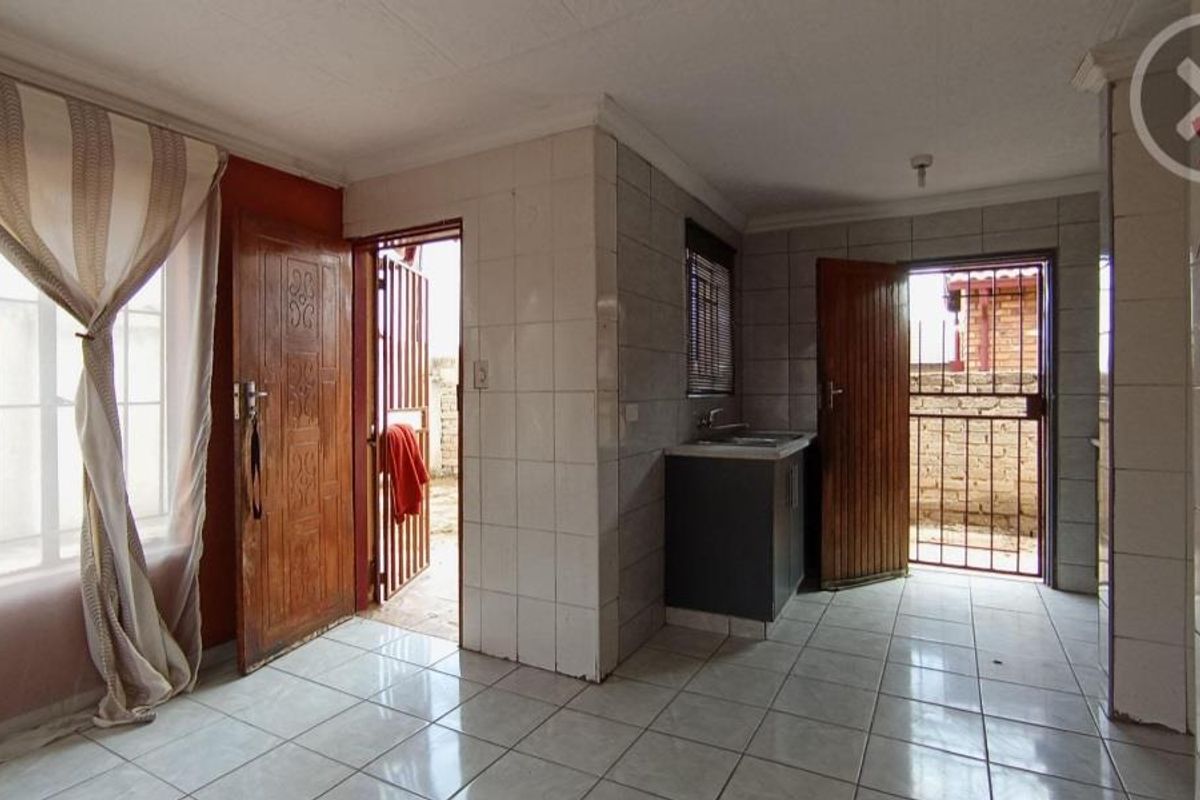A functional kitchen area featuring tiled walls and flooring, built-in cabinetry with a sink, and direct access to the exterior via security gates.