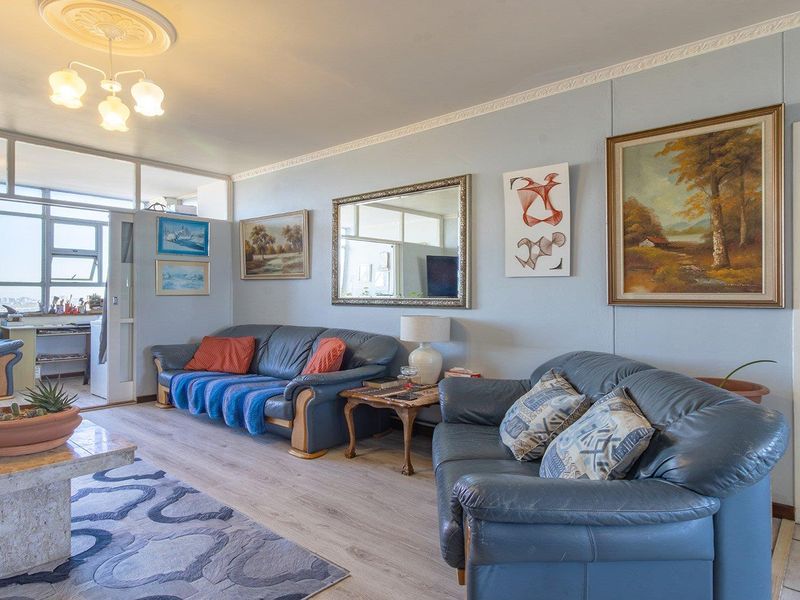 A spacious living room featuring laminate flooring, decorative crown molding, a ceiling rose, and an internal glass partition leading to an enclosed balcony area.