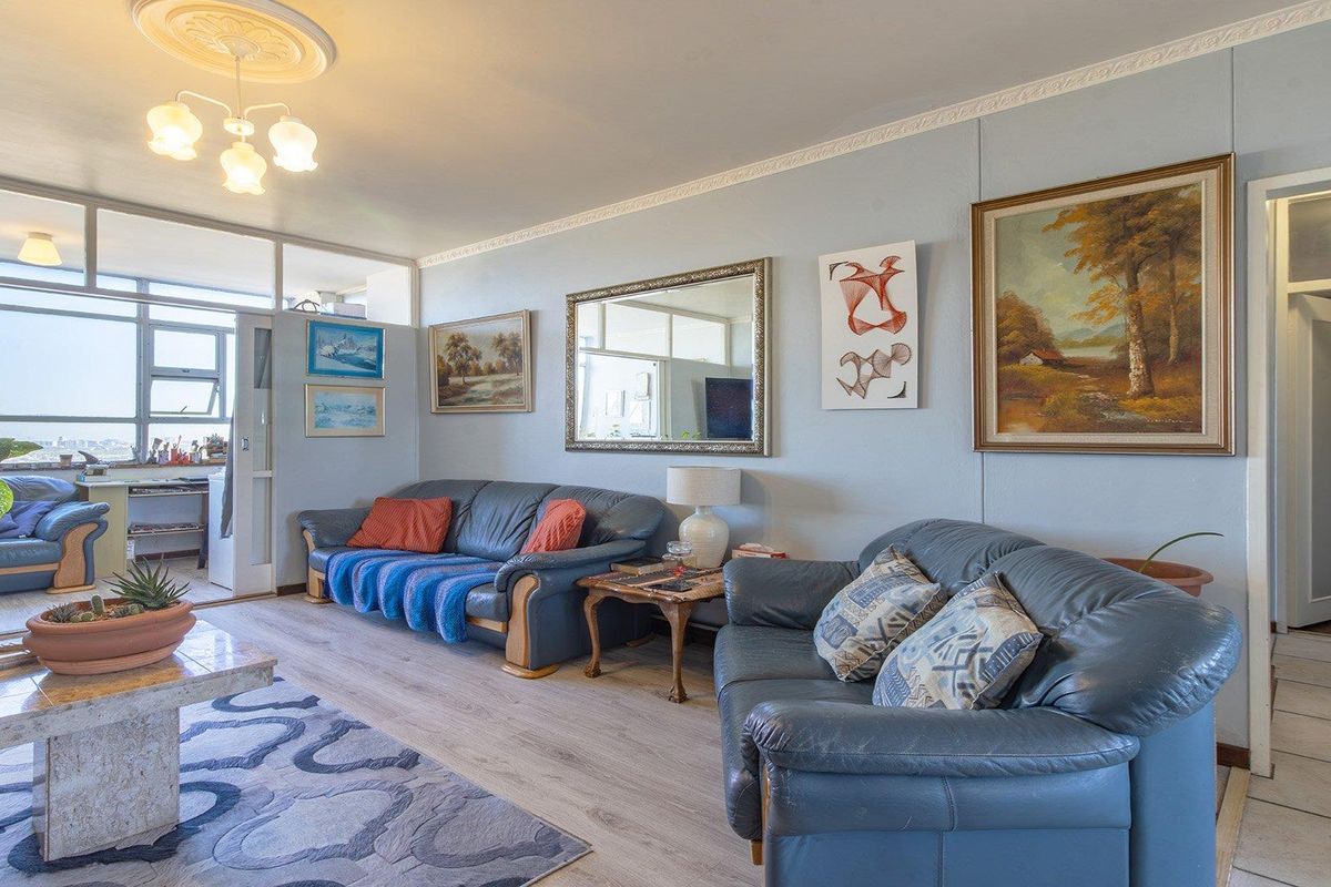 A spacious living room featuring laminate flooring, decorative crown molding, a ceiling rose, and an internal glass partition leading to an enclosed balcony area.