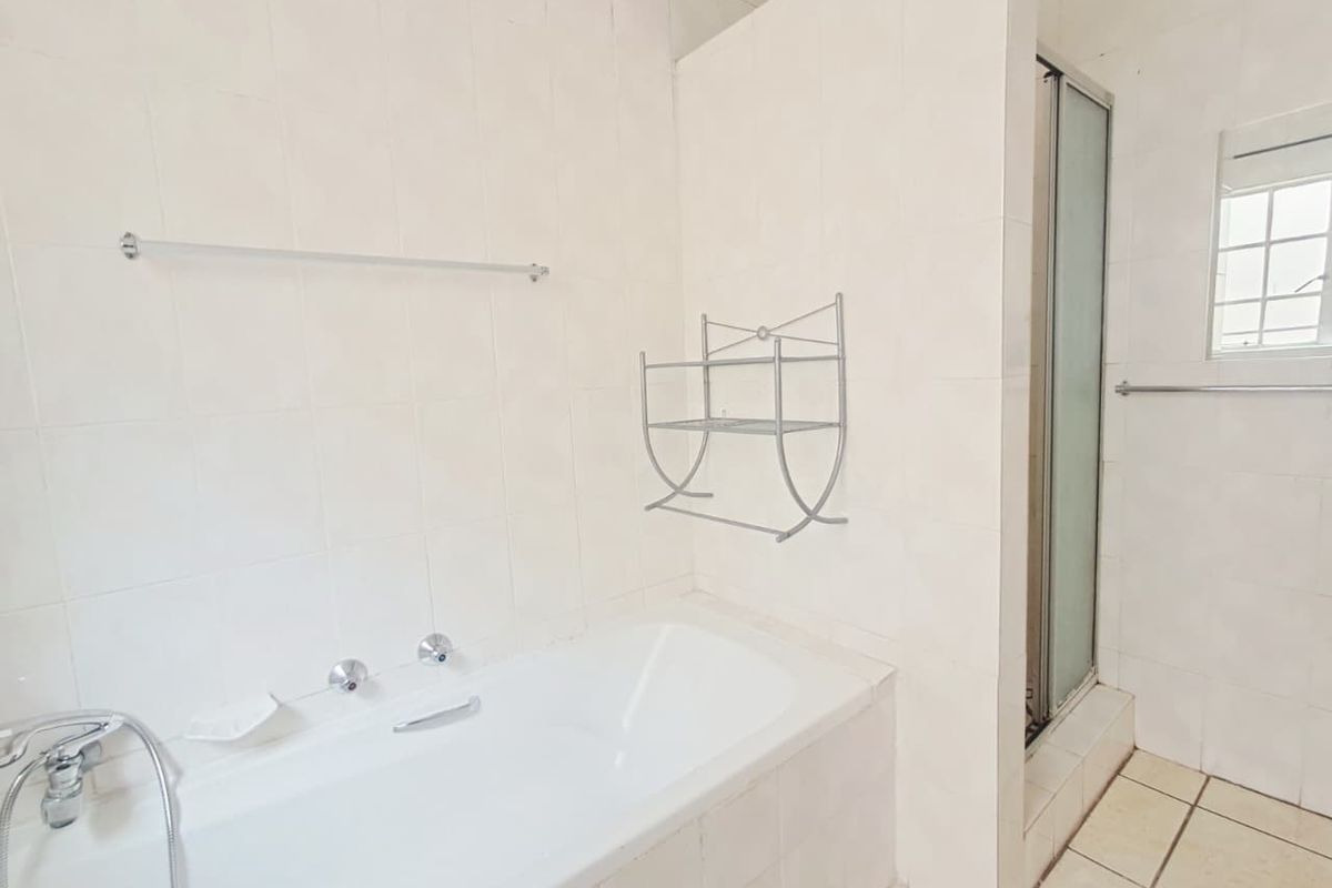 A functional bathroom featuring a built-in bathtub, separate shower enclosure, and neutral ceramic tiling throughout.